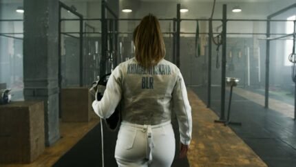 Back view of a female fencer preparing for training in a modern indoor gym.